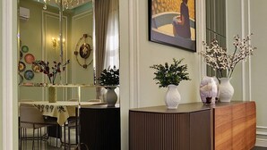 Un interno moderno con una consolle in legno, un lampadario e una zona pranzo visibile attraverso uno specchio.
