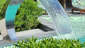 Area piscina esterna moderna con elemento d'acqua limpida, circondata da verde curato e un edificio contemporaneo sullo sfondo.