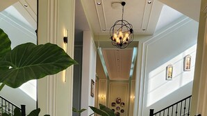 Un elegante ingresso in marmo con scalinata, grandi piante in vaso e un lampadario.