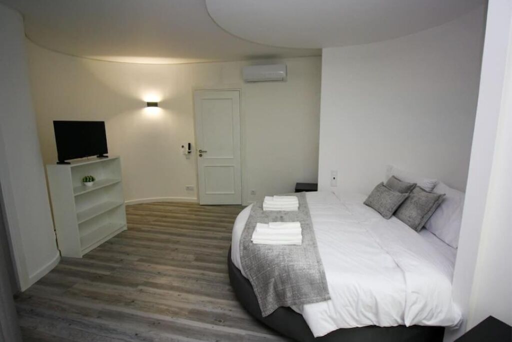 A bedroom with a bed, a TV on a shelf, a door, and a wall-mounted air conditioner.
