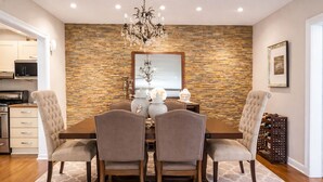 Un comedor con pared de piedra, una araña y una cocina al fondo.