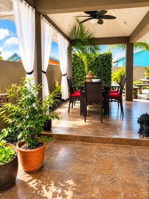 Un patio exterior con una mesa y sillas, rodeado de plantas en macetas y vistas a un edificio azul.