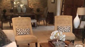Una sala de estar con un sofá, dos sillones, una mesa de centro y un comedor al fondo.