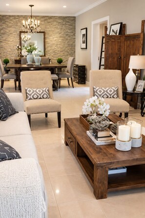 Una sala de estar con un sofá, dos sillones, una mesa de centro con objetos decorativos, un comedor con mesa y sillas, y una pared de acento de piedra.