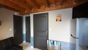 Un couloir avec un plafond en bois, un canapé noir et un réfrigérateur.