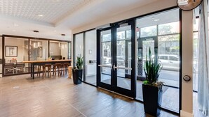 Een moderne hotel lobby met een receptiebalie, zithoek en grote glazen deuren naar de straat.