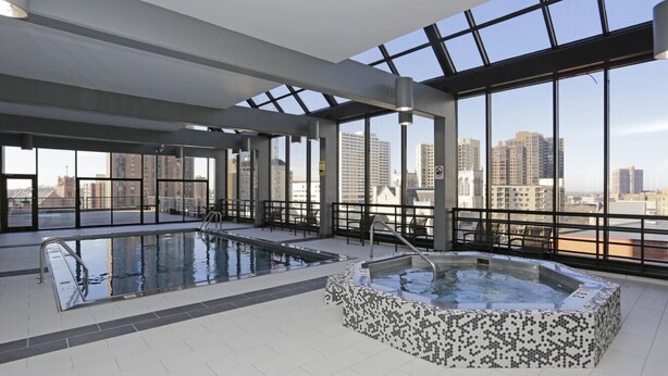 A modern indoor pool area with a hot tub, large windows, and a city view. - Downtown  2bd  Sky Lounge  Pool  Gym  Q (Minneapolis)
