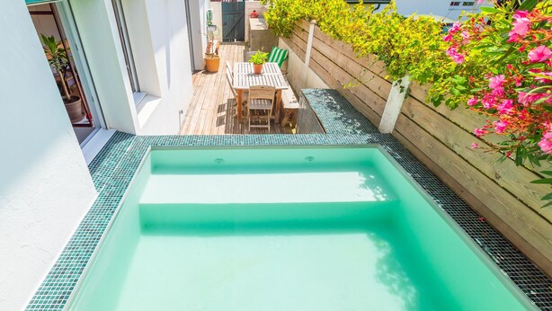 Una piscina en la azotea con terraza de madera y una mesa con sillas.
