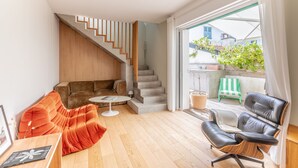 Un salón moderno con una escalera, un sofá, una mesa de centro y vistas al exterior.