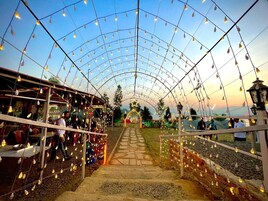 Uma galeria coberta com luzes de corda, que leva a um arco decorado e tendas ao longe.