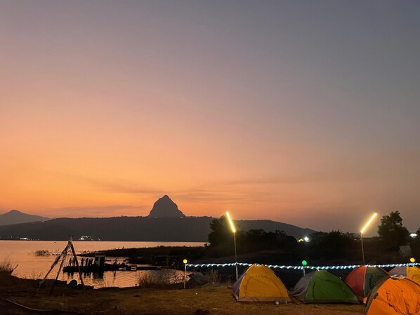 Un terrain de camping au crépuscule, avec des tentes et un quai au bord de l’eau.