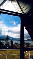 Vista pela janela, com moldura de metal, céu claro e um corpo de água com montanhas ao longe.