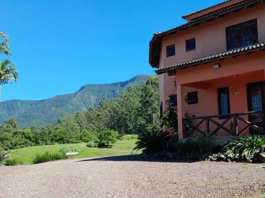 A two-story building with a balcony, surrounded by palm trees and greenery, with mountains in the background.
