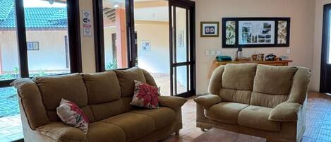 A living room with two sofas and a coffee table, large windows, and a tiled floor.