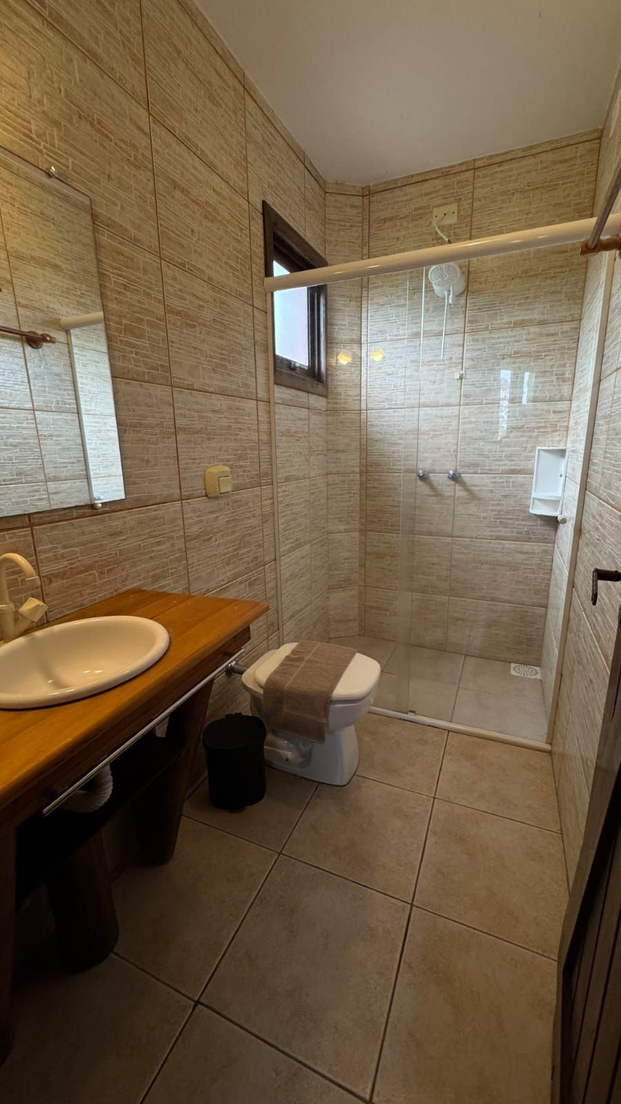 Bany modern amb un envà d'aigua de fusta, un lavabo blanc, un vàter i una zona de dutxa amb vidre.