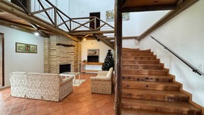 A spacious living area with a stone fireplace, a wooden staircase, and a Christmas tree.