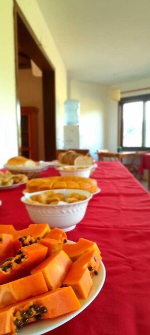 A buffet table with various dishes, including a plate of sliced mango in the foreground. - Refúgio Rio do Boi (Praia Grande)