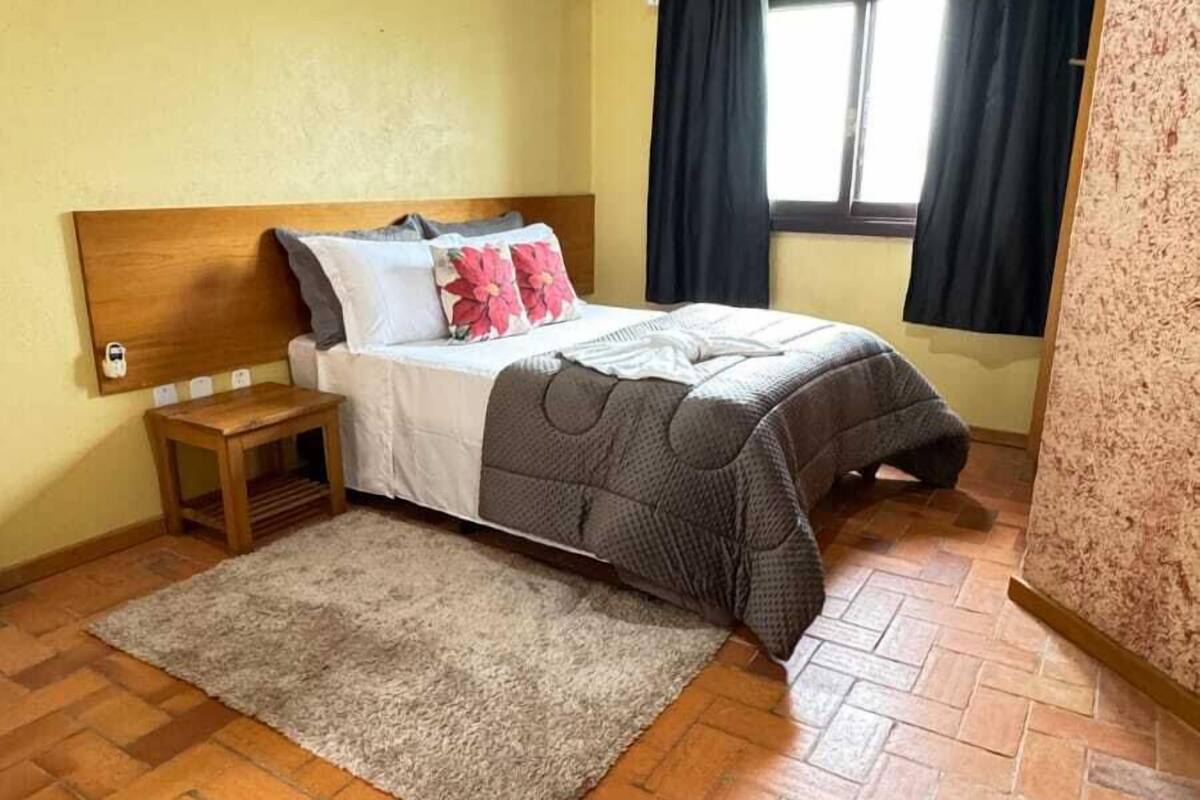 A bedroom with a bed, a nightstand, a rug, and a window with curtains.