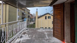 A balcony with a metal railing, a concrete floor, and a view of neighboring buildings. - Cozy 2nd floor apartment with terrace (Venezia)