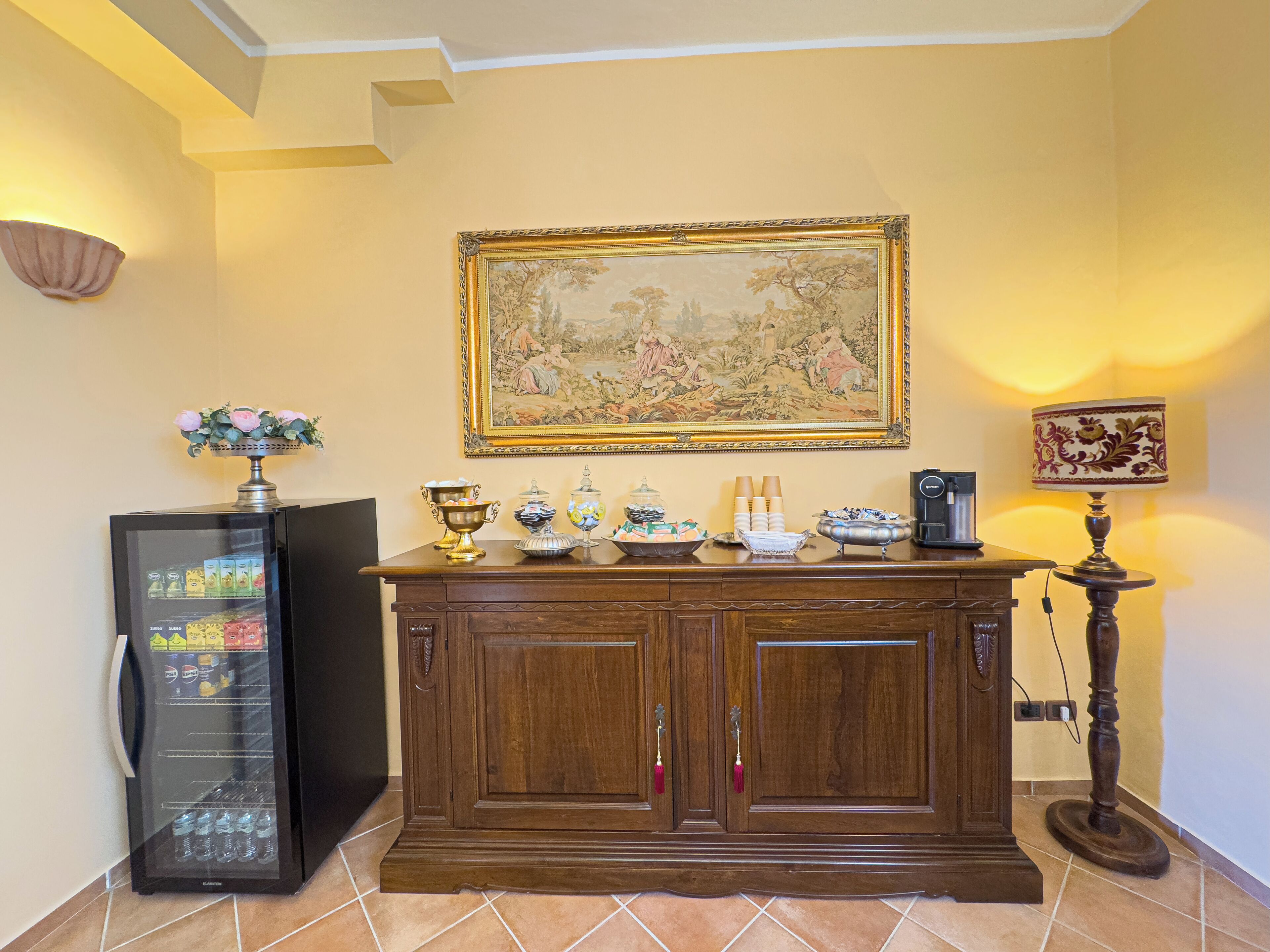 Een kamer met een houten kast, een schilderij, een vaas met bloemen, een koffieapparaat en een drankenspender.