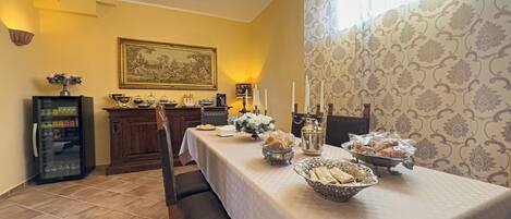 A dining area with a long table set for a meal, a chandelier, a cabinet with decorative items, and a patterned wallpaper wall.