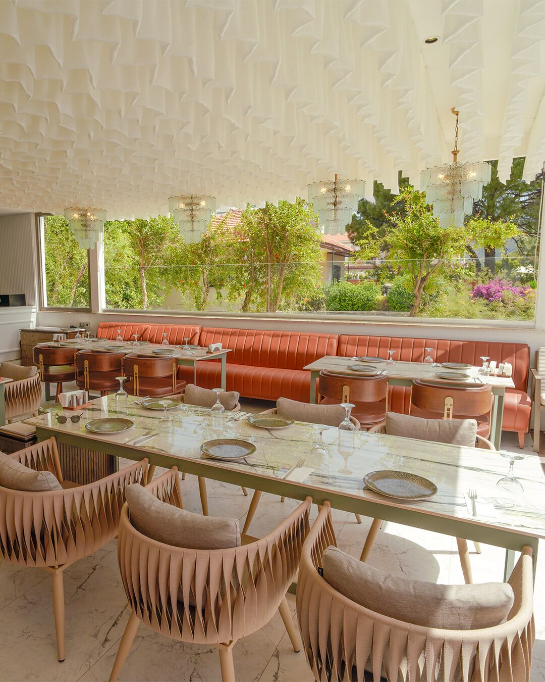 Un restaurante con una larga mesa dispuesta para comer, asientos con cojines y vistas a espacios verdes.