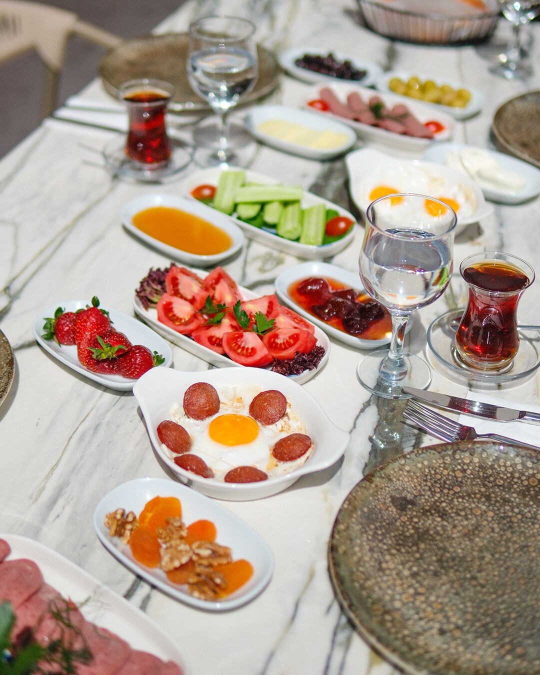 Uma mesa posta com diversos pratos, incluindo tomates fatiados, morangos e um prato com ovos e pepperoni.