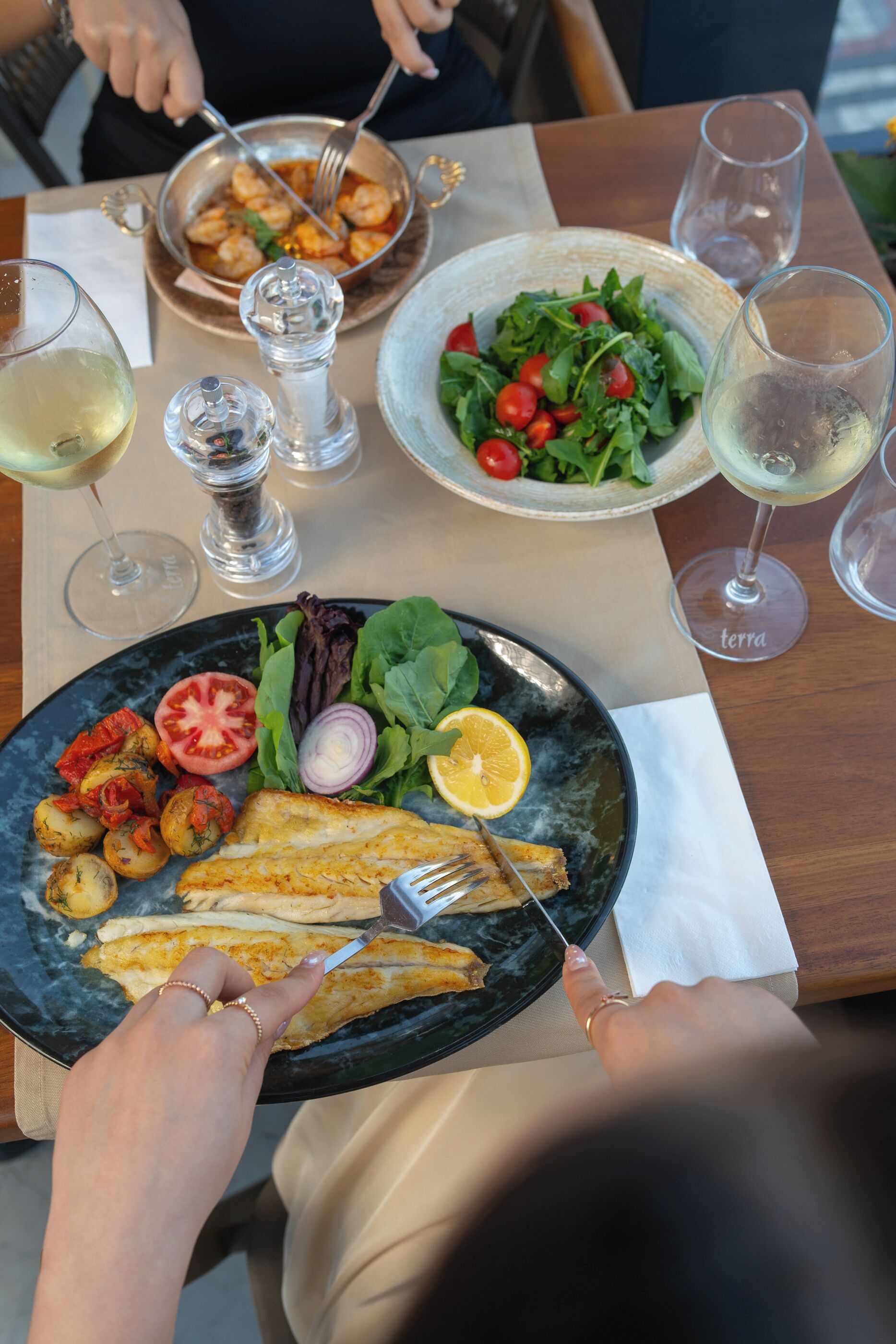 Une table à manger avec des assiettes remplies de nourriture, des verres de vin et un salier et un poivrier.