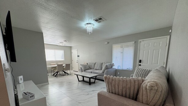 A modern living room with a sofa, a coffee table, and a TV. There is a dining area with chairs and a table. The room has a chandelier and a door. - Charming 3-bedroom Private Home in the Heart of Sacramento (Sacramento)