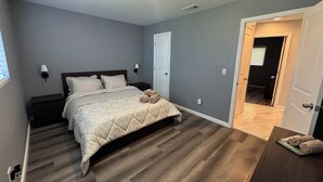 A bedroom with a bed, a nightstand, a wall-mounted lamp, and a door leading to another room. - Charming 3-bedroom Private Home in the Heart of Sacramento (Sacramento)