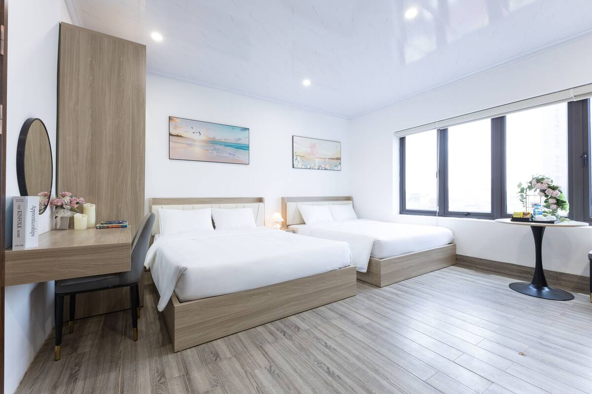 Ett modernt hotellrum med två sängar, ett skrivbord och ett stort fönster.