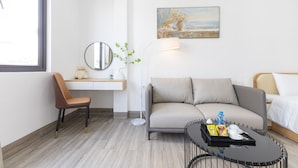 Una habitación de hotel moderna con sofá, un escritorio pequeño, una silla, una mesita de centro y un cuadro en la pared.