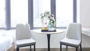 Habitación de hotel con dos sillones blancos, una mesa redonda con una bandeja de alimentos para el desayuno y un jarrón de flores rosas.