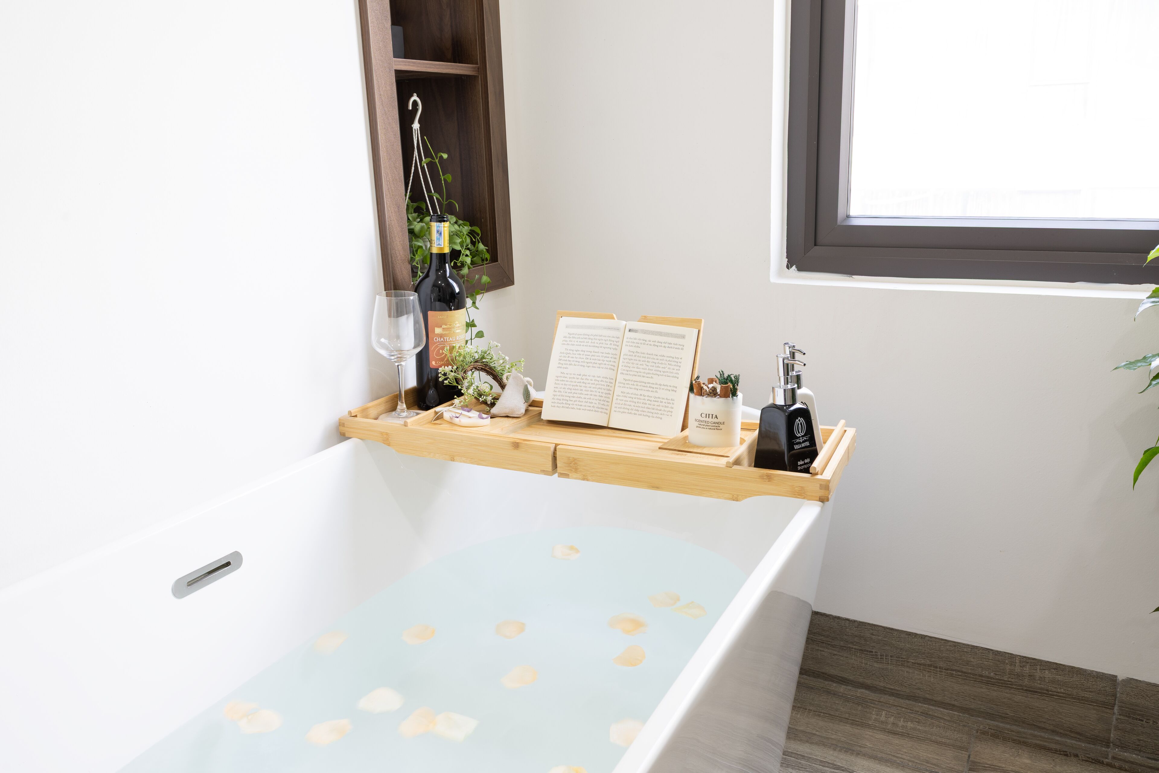 Une salle de bain avec une baignoire, une étagère en bois sur laquelle se trouvent une bouteille de vin, une bougie et un livre.