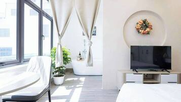 A modern hotel room with a bed, a TV, a seating area, and a potted plant.
