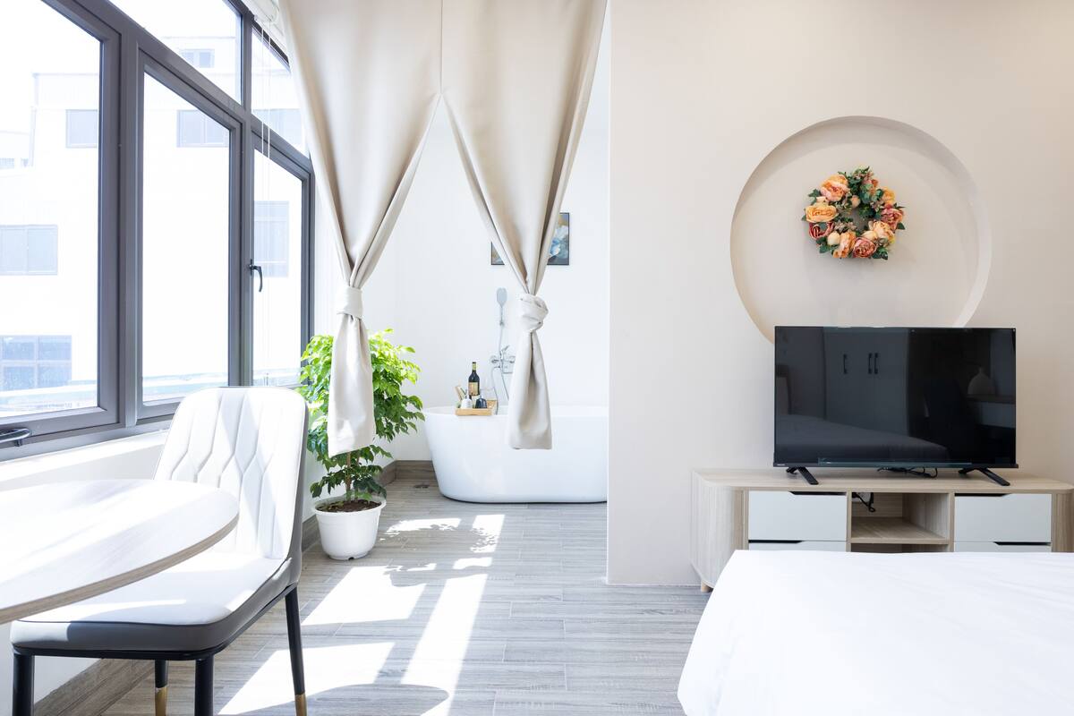 Ett modernt hotellrum med ett stort fönster, ett vitt badkar, en platt-TV och en krukväxt.