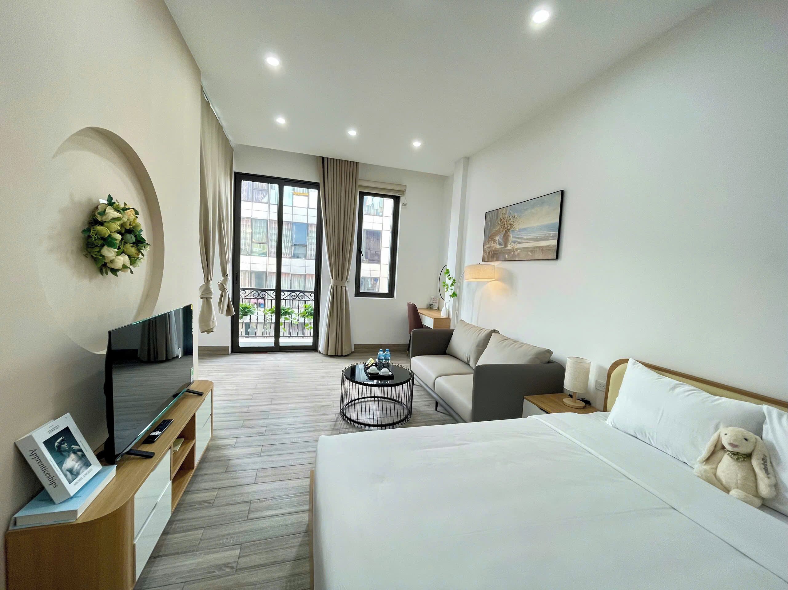 A hotel room with a bed, a sofa, a TV, a desk, and a balcony with curtains.