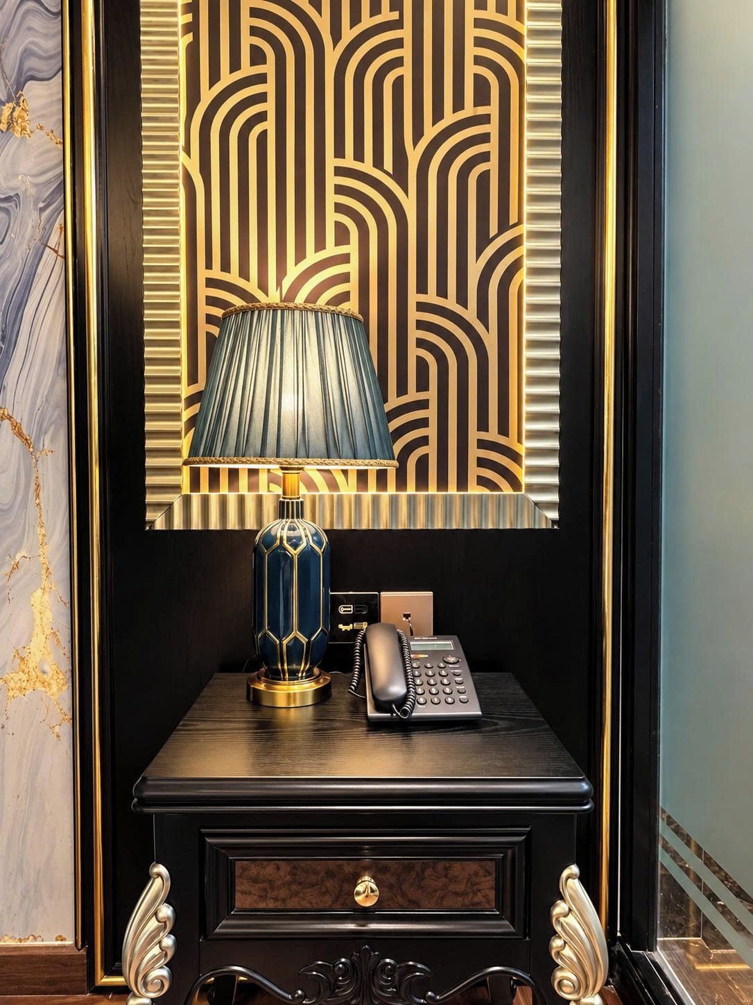 Un bureau avec une lampe, un téléphone et un panneau décoratif orné de motifs géométriques.