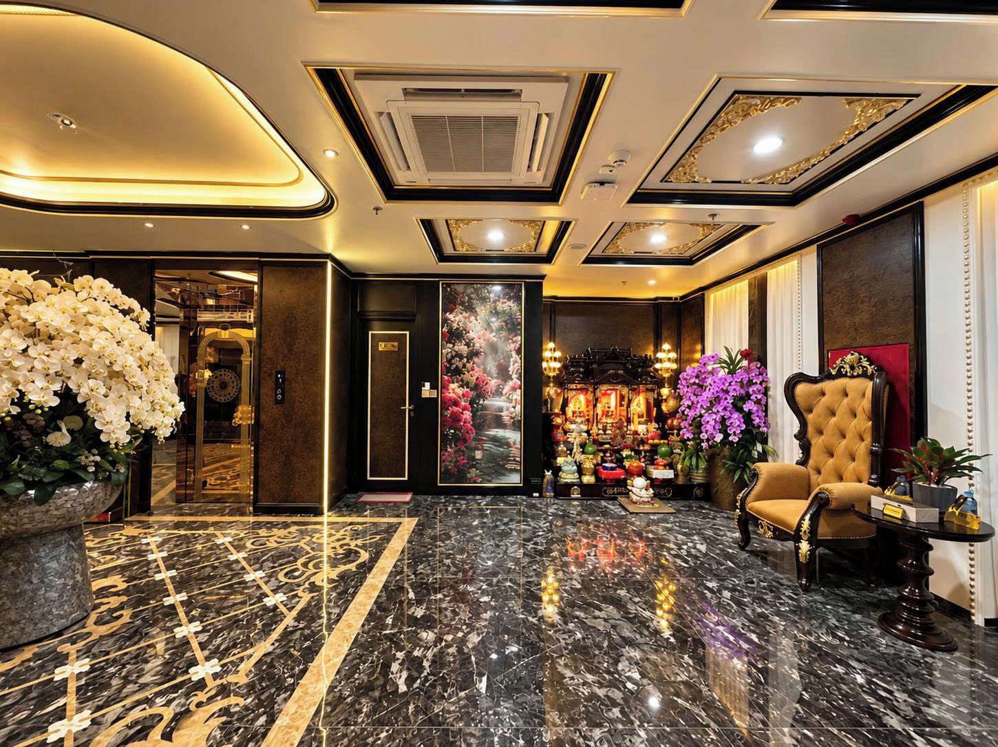 A lobby with a marble floor, a reception desk, a large floral arrangement, and a traditional altar with offerings.