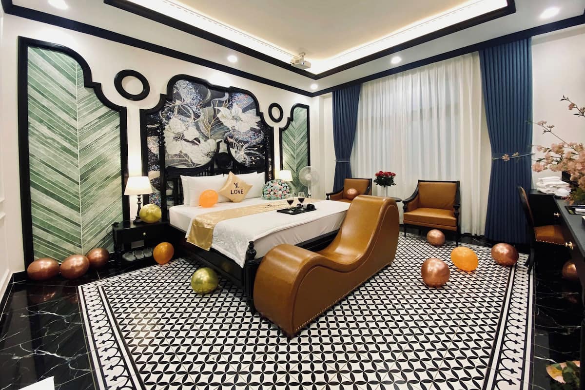 Ein modernes Hotelzimmer mit einem großen Bett, einem Schreibtisch und einem Stuhl. Der Raum verfügt über einen gemusterten Boden und dekorative Elemente an den Wänden.