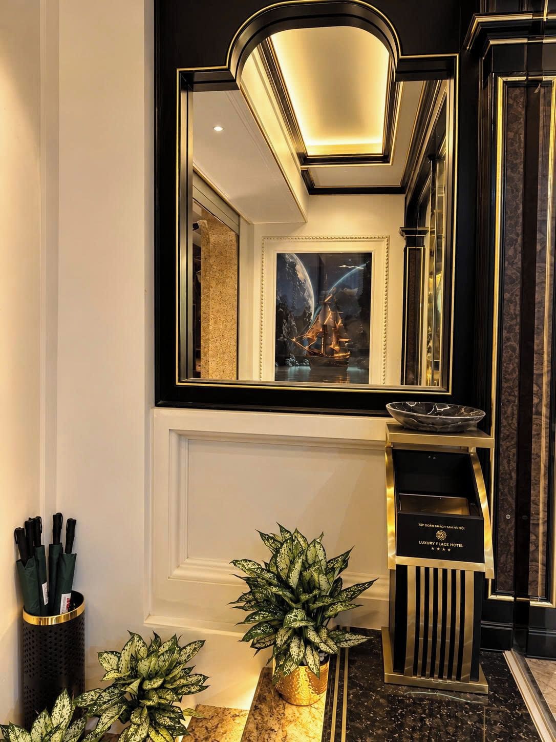 Un lobby de hotel lujoso con un espejo grande, una obra de arte enmarcada y un cuenco decorativo sobre un pedestal.