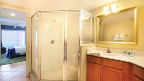 Un baño de hotel con ducha de vidrio, lavamanos con espejo y armarios de madera.