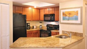Una cocina con gabinetes de madera, encimera de granito, refrigerador negro, microondas, estufa y pileta.
