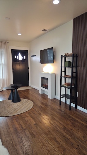 A living room with a fireplace, a television mounted on the wall, a round table with a rug, and a bookshelf.