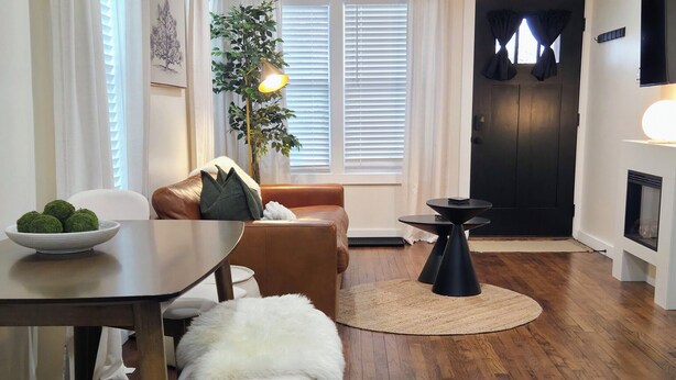 Una sala de estar moderna con comedor, piso de madera, chimenea y un ventanal con cortinas.