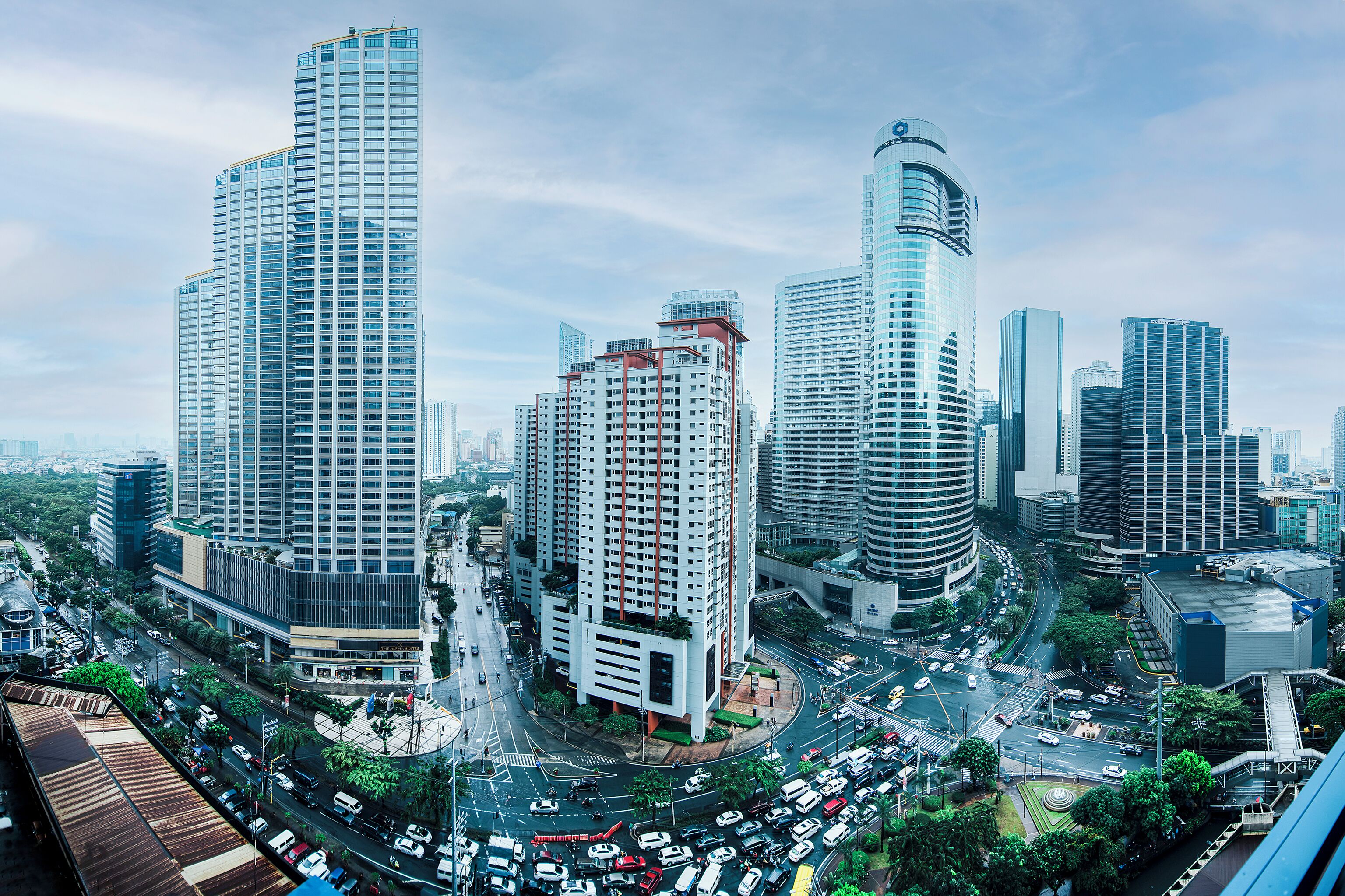 Un quartier urbain dense, avec de hauts gratte-ciel modernes, une intersection animée et un mélange de bâtiments commerciaux et résidentiels.