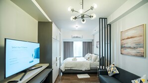 Ein modernes Hotelzimmer mit Flachbildfernseher, einem Bett mit weißer Bettwäsche, einem dunkelgrauen Sofa und einem großen Gemälde an der Wand.