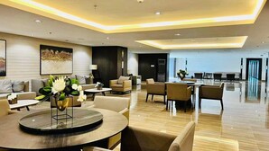 Eine geräumige Lobby mit einem runden Tisch, Sofas und Sesseln, gestaltet im modernen Stil mit eingelassener Beleuchtung und einem großen Kunstwerk an der Wand.