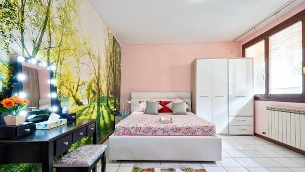 Un dormitorio con cama, tocador con espejo e iluminación, escritorio y ventana.
