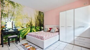 Un dormitorio con cama, tocador con luces, armario y un mural de un bosque.